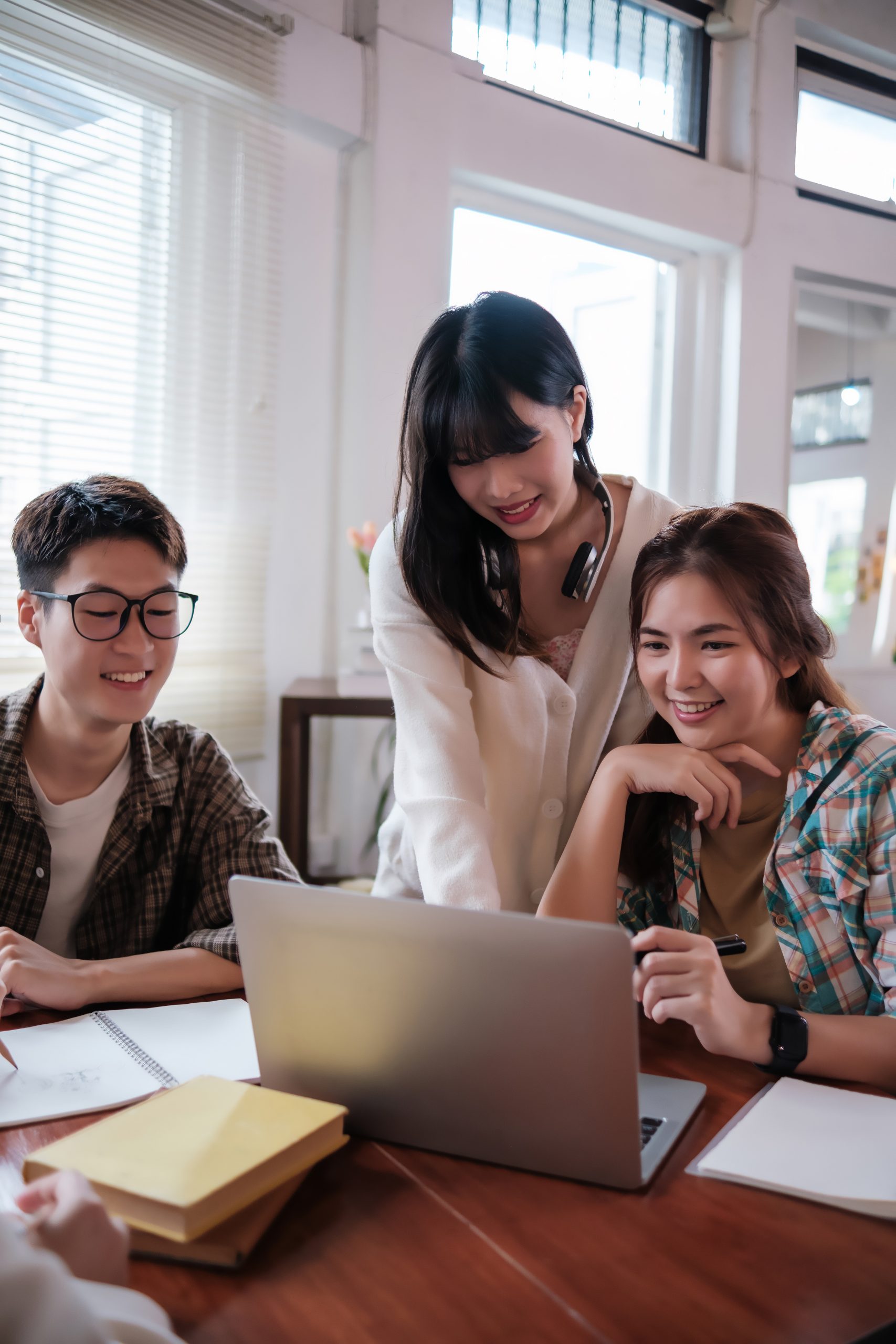 Cheerful and smart young Asian male college student is tutoring math to his friends in a school.
